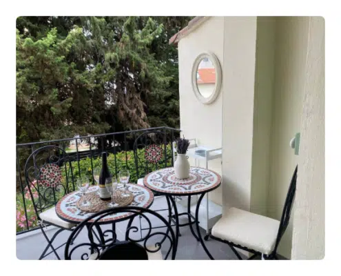 LocationKeasy - Havre de paix · terrasse au coeur du vieil Antibes Un balcon accueillant avec deux tables en mosaïque, du vin, des verres et un vase de lavande. Des chaises en fer forgé et une végétation luxuriante créent une atmosphère sereine et chaleureuse.