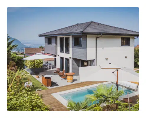 keasy location - Villa SérénAlp Maison moderne à deux étages avec façade grise et blanche, piscine à l'arrière, mobilier de terrasse et jardin paysager sous un ciel bleu azur.